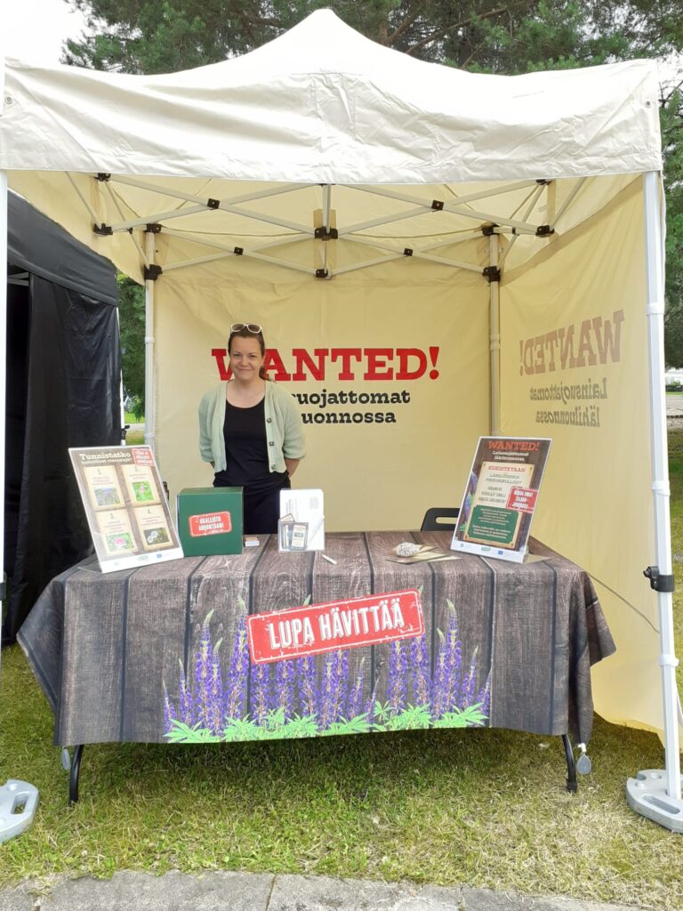 Nainen seisoo ständillä jossain kesäisessä ulkoilmatapahtumassa.