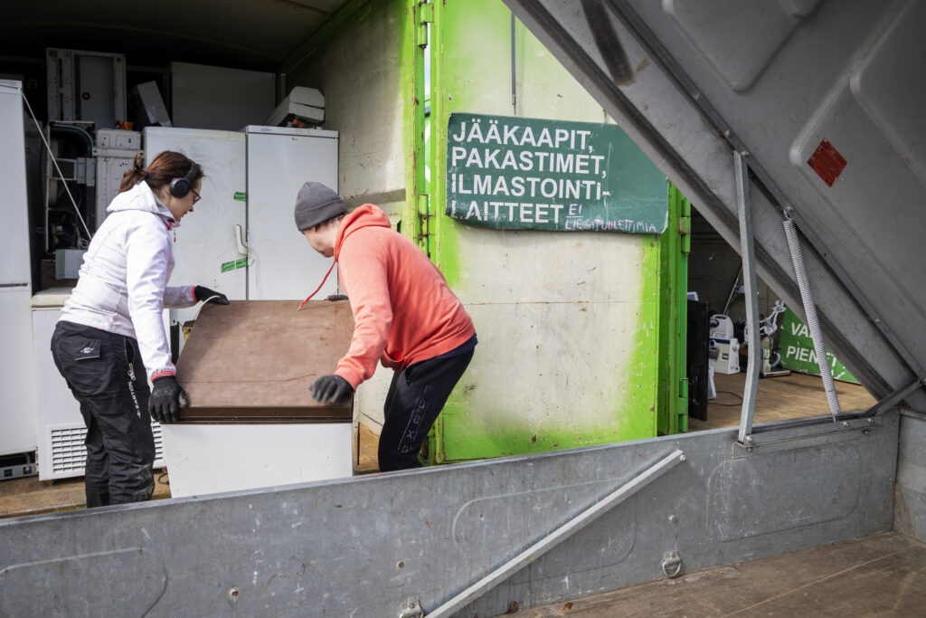 Nainen ja mies tuovat sähkölaitetta Mustankorkean jätekeskukselle.