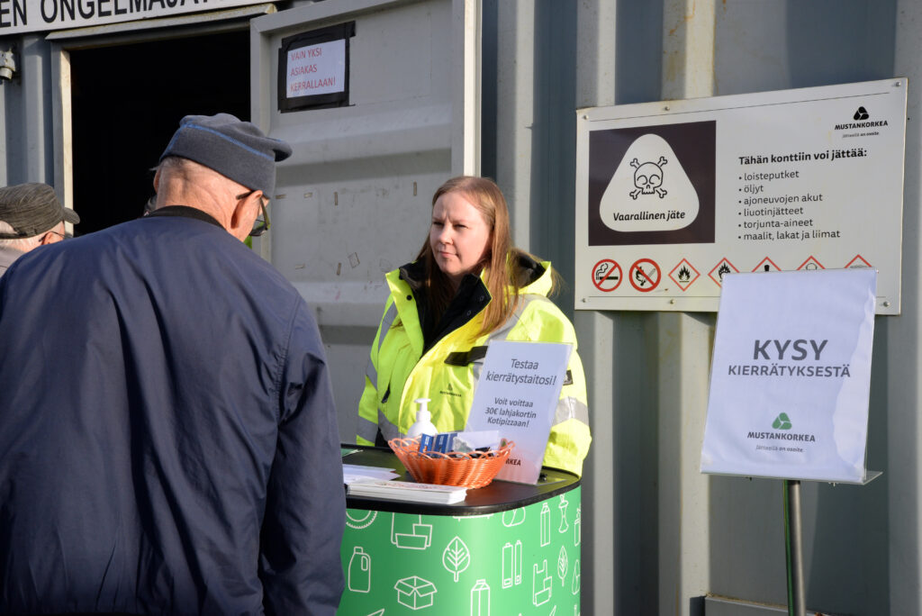 Mies kysyy kierrätyskoutsilta kierrättämisestä, kierrätyskoutsi kuuntelee tarkkaavaisena