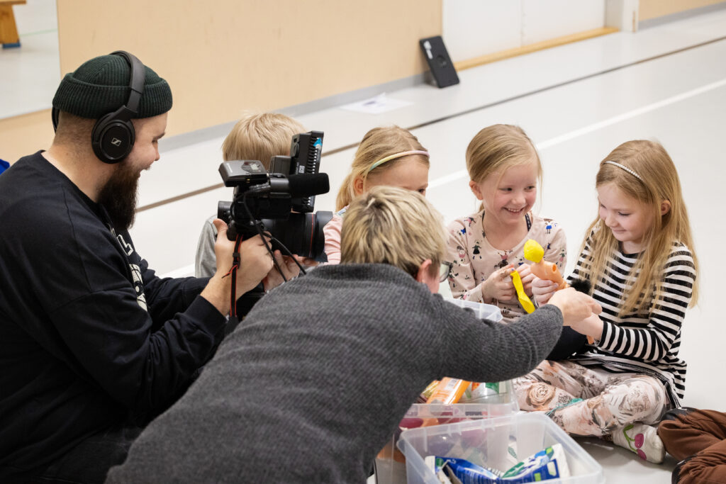 Mies videokuvaa ja nainen haastattelee eskari-ikäisiä lapsia