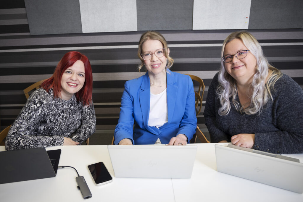 Kolme naista istuu pöydän äärellä neuvotteluhuoneessa