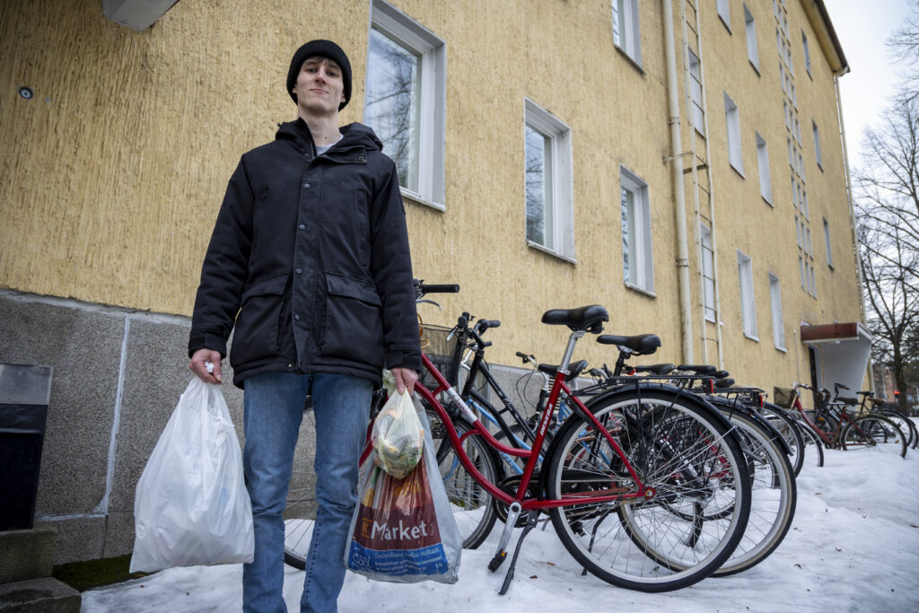 Nuori mies seisoo kerrostalon pihassa kolmen roskapussin kanssa