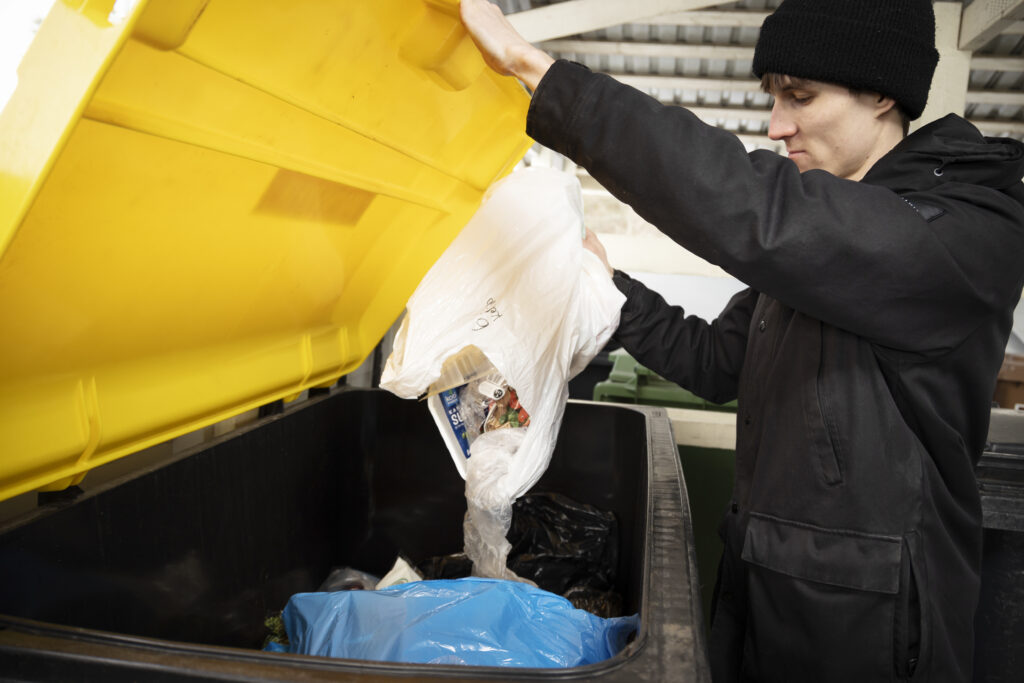 Nuori mies laittaa tyhjentää muovipakkauksia jäteastiaan