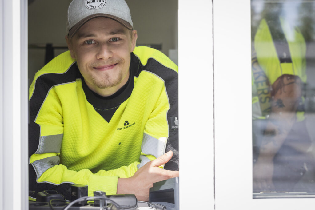 Nuori kesätyöntekijä katselee kassakopin ikkunasta hymyillen