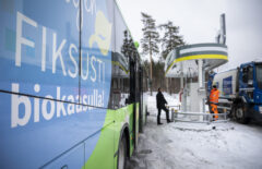 Bussin kyljessä on "Kuljen fiksusti biokaasulla" -tarra, taustalla näkyy kaksi miestä tankkaamassa Seppälän tankkausasemalla
