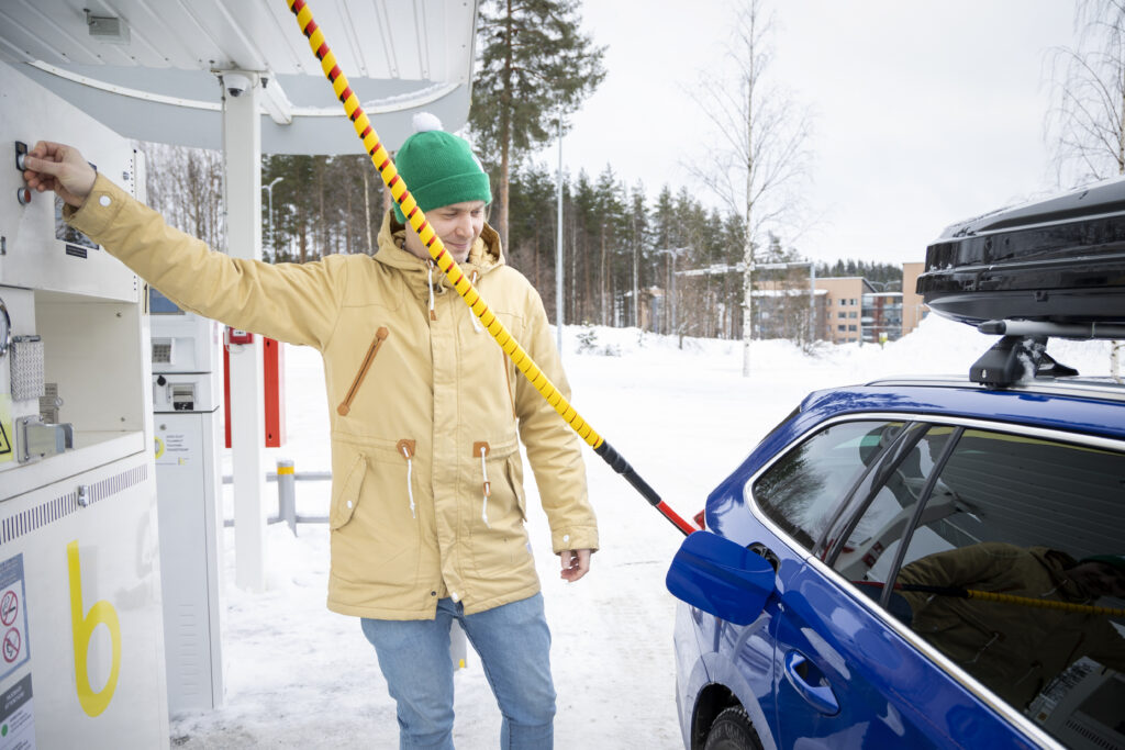 Keltatakkinen mies tankkaa talvella autoonsa biokaasua