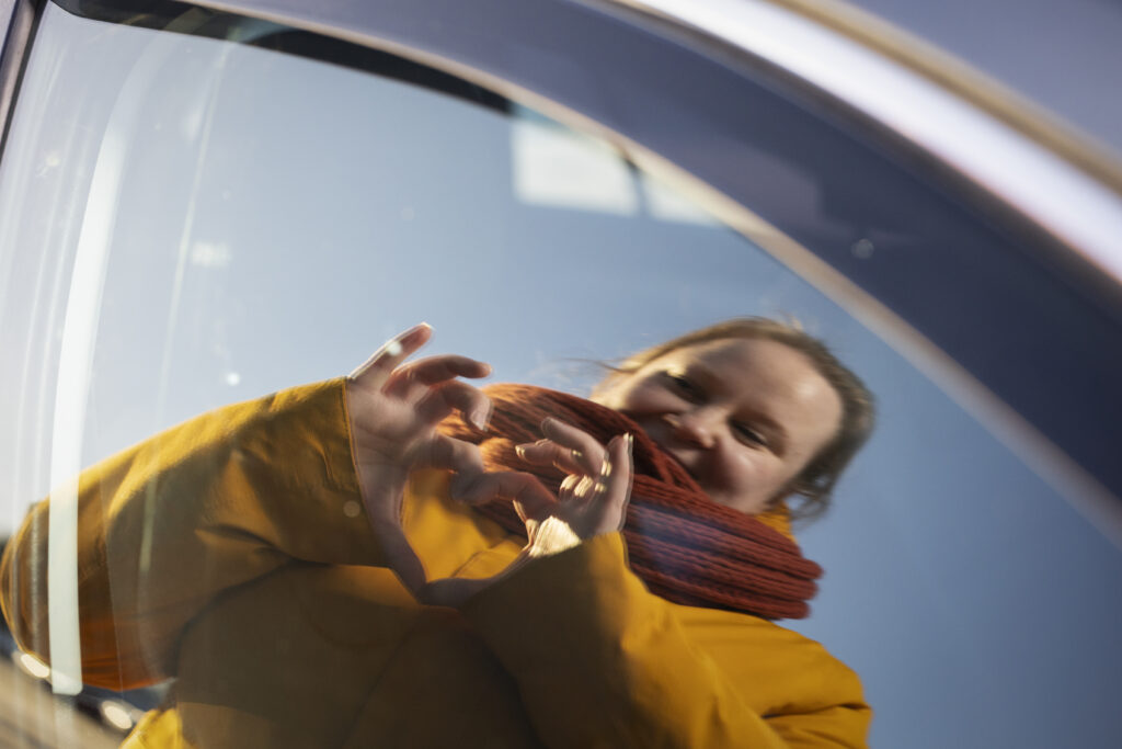 Nainen näyttää käsillään sydäntä, joka heijastuu auton ikkunasta