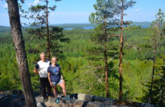 Mies ja nainen seisovat komeissa maisemissa Hyyppäänvuorella, alhaalla näkyy puita ja järveä.