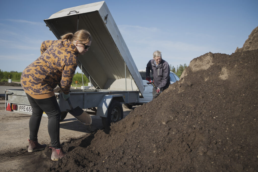 Nainen ja hänen isänsä lapioivat multaa Jyväskylän Omapihalla peräkärryn kyytiin.