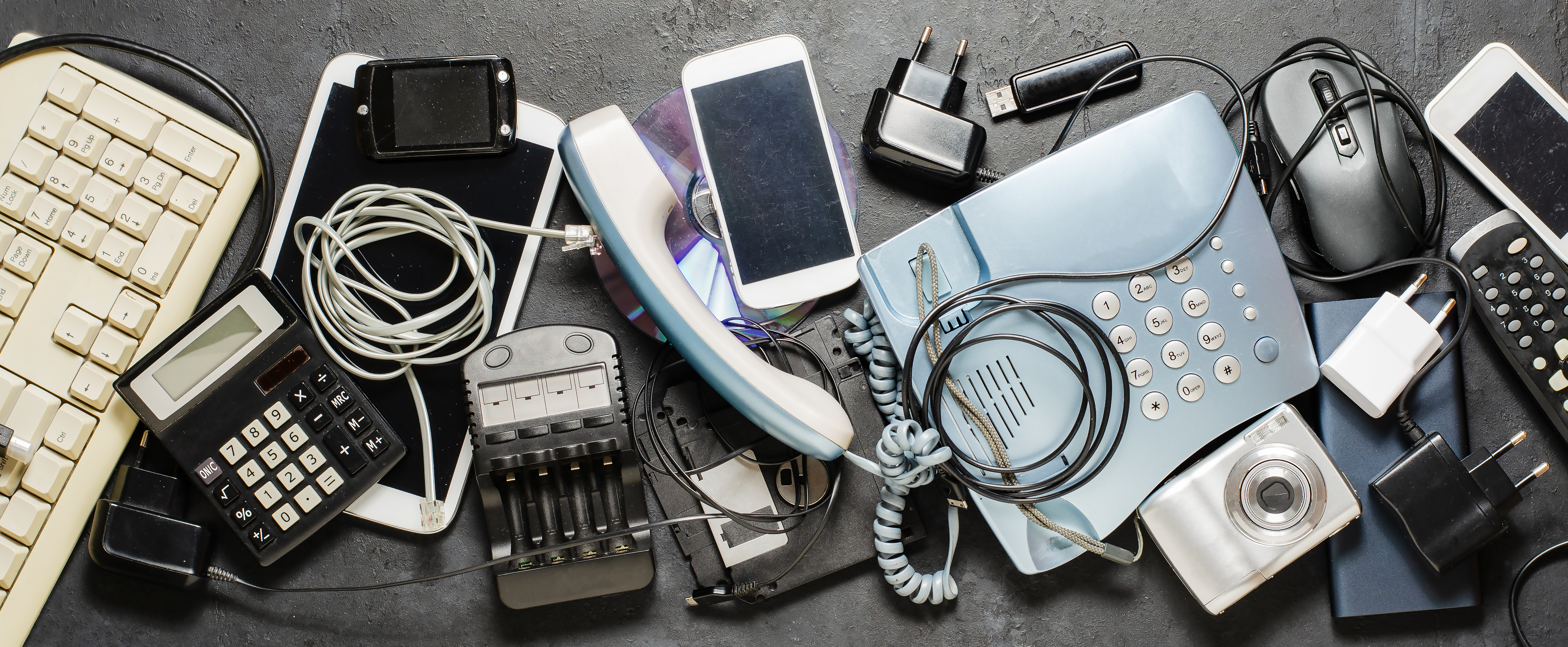 Kuvassa sähkölaitteita, muun muassa kännyköitä, vanhoja puhelimia, latureita, laskin ja näppäimistö.