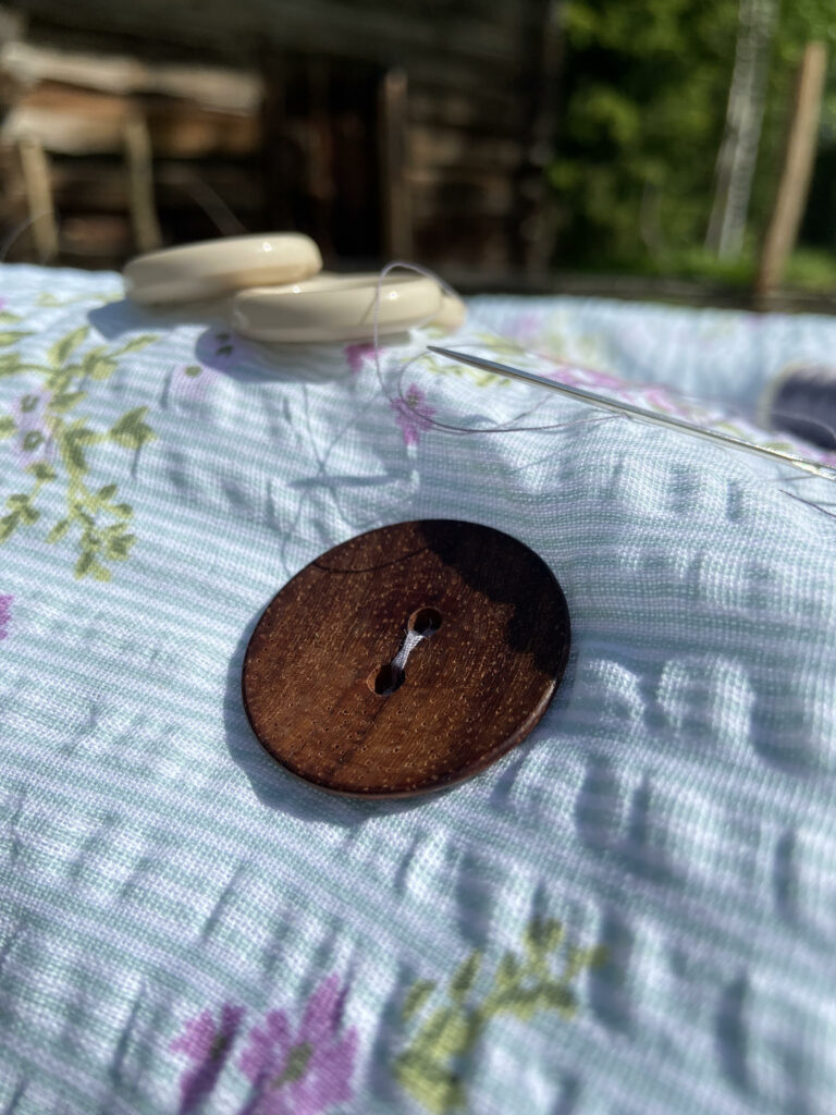 Lähikuvassa ruskea nappi, joka ommellaan kiinni vanhasta lakanasta tuunattuun istuintyynyyyn