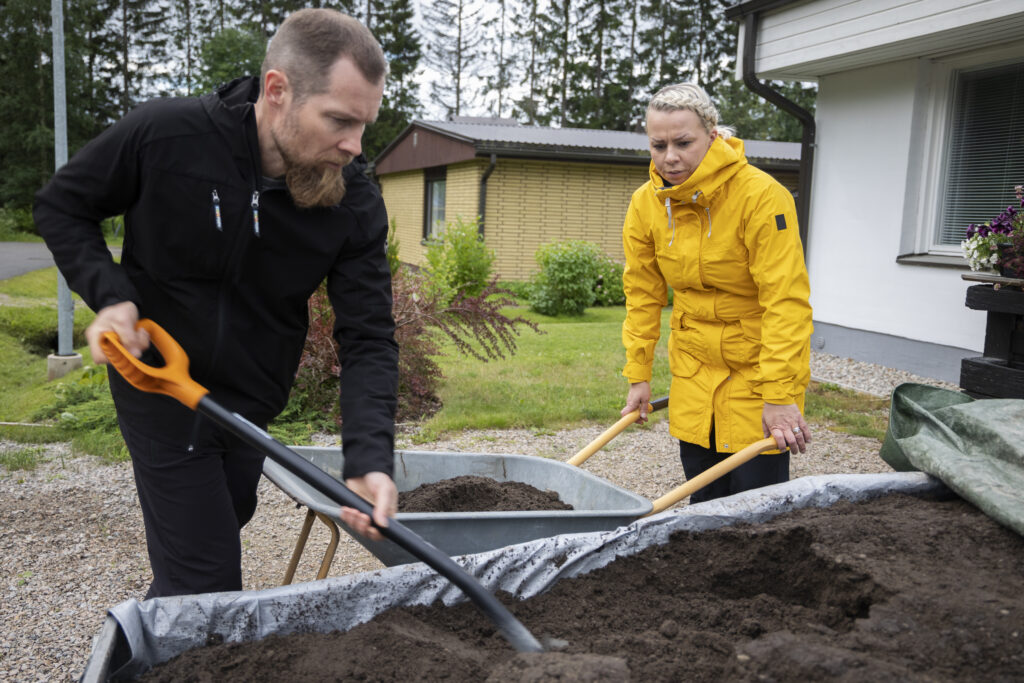 Mies ja nainen lapioivat multaa peräkärrystä kottikärryyn.