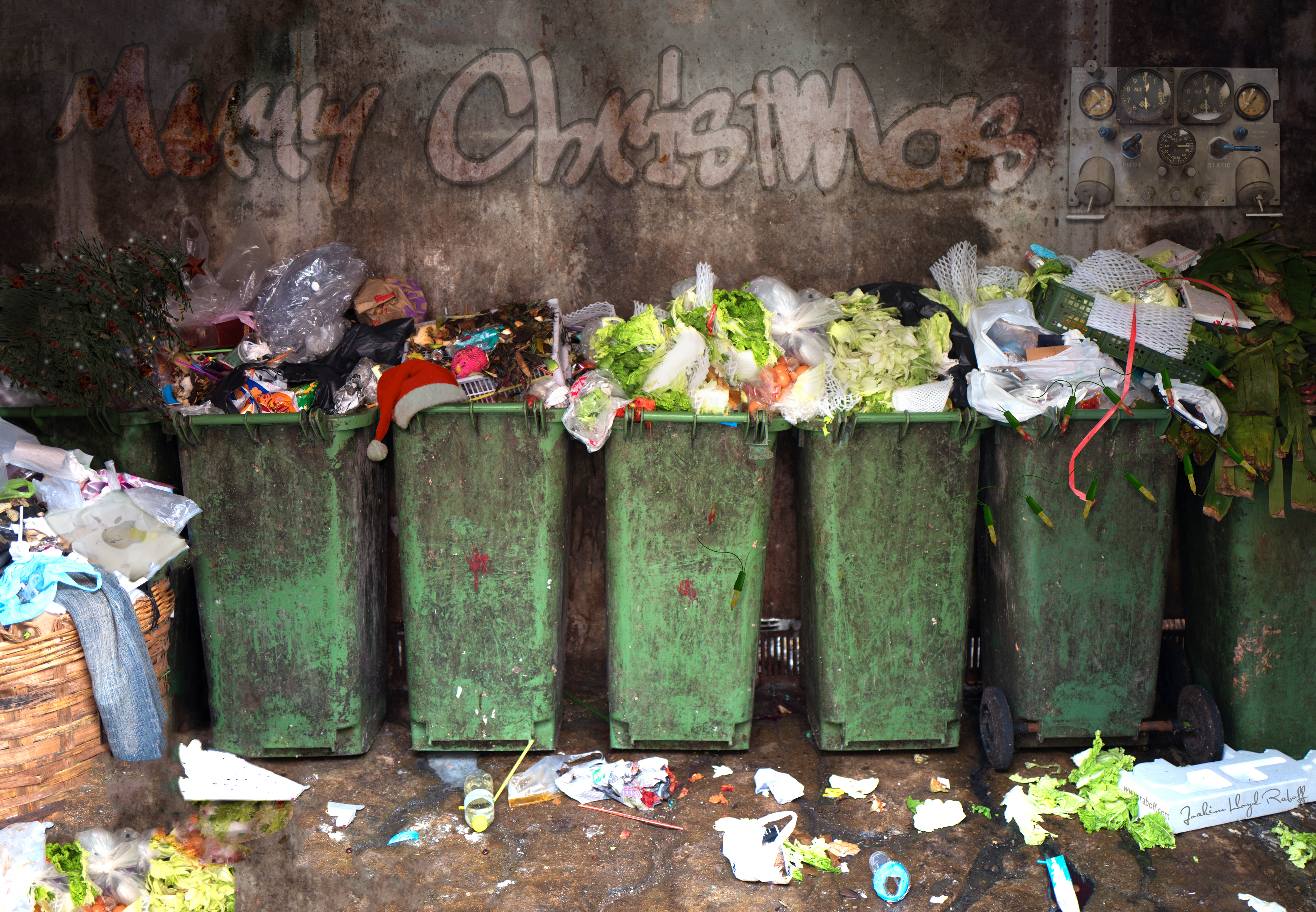 Vihreät jäteastiat pursuavat joulun ajan jätteitä inhottavasti. Seinässä lukee graffitein "merry christmas".