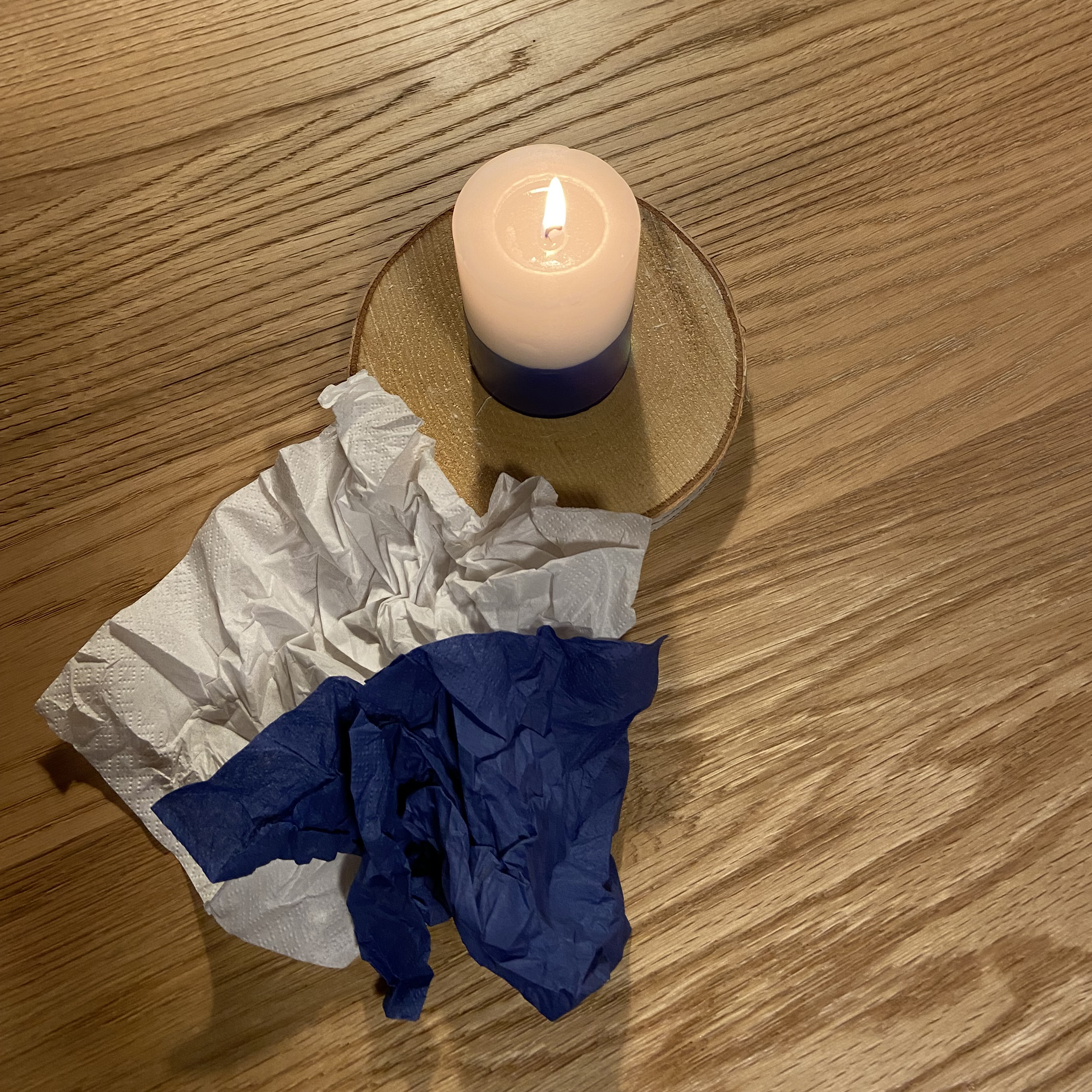 Sinivalkoinen ruokaservetti tammipöydällä, vieressä palaa sinivalkoinen kynttilä.
