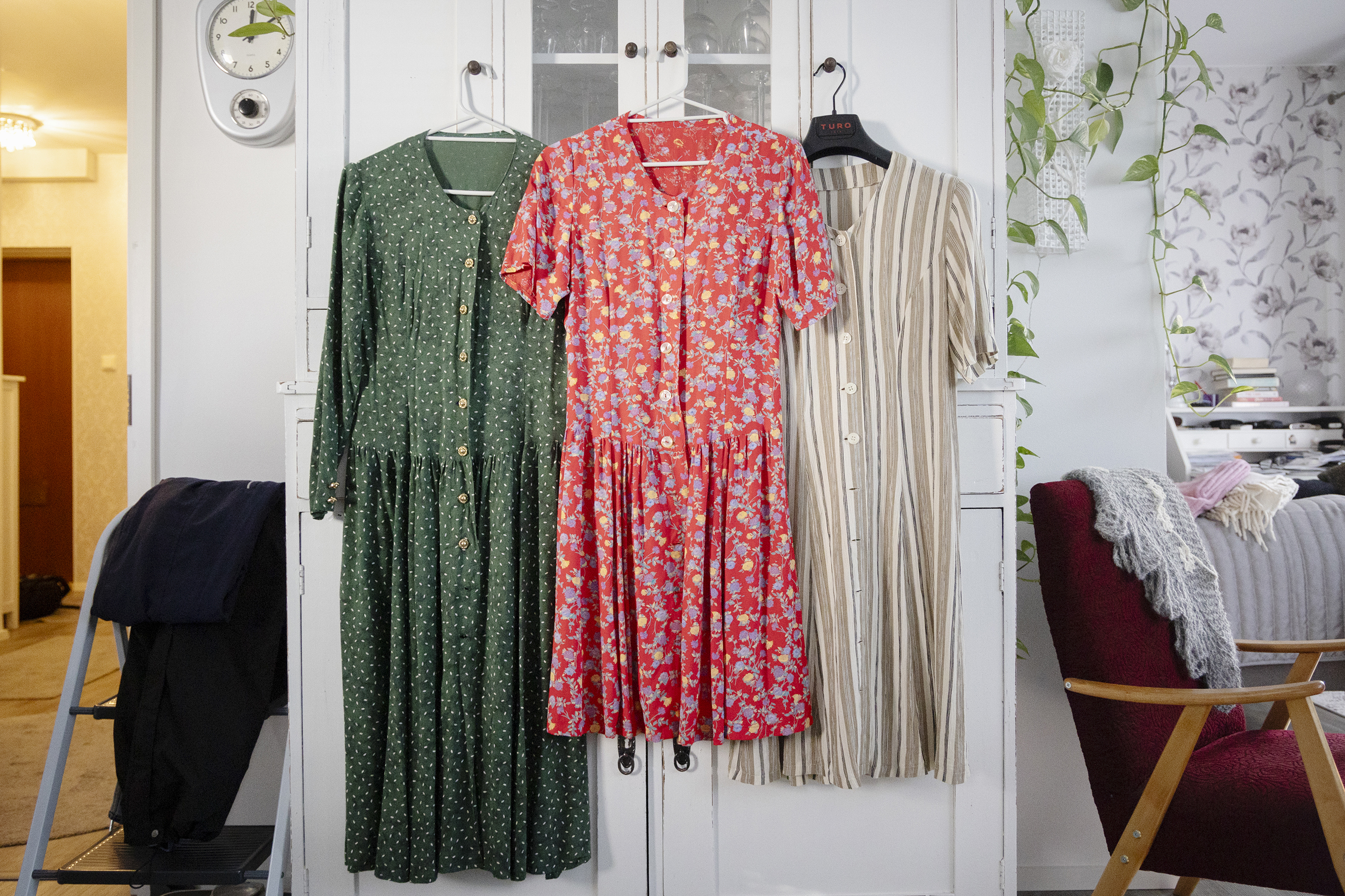 Olohuoneen kaapistosta roikuu kolme erilaista mekkoa; vihreäpilkullinen, punakukkainen ja ruskearaidallinen.