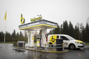 Biokaasuauto on pysähtyneenä Mustankorkean jätekeskuksen tankkausasemalla. Myös pakettiautossa on biokaasun keltaiset tarrat. Sää on melko harmaa ja sateinen.