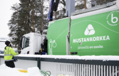 Mustankorkean jäteauto tyhjentää isoa syväkeräysastiaa. Etualalla näkyy roskiksia.