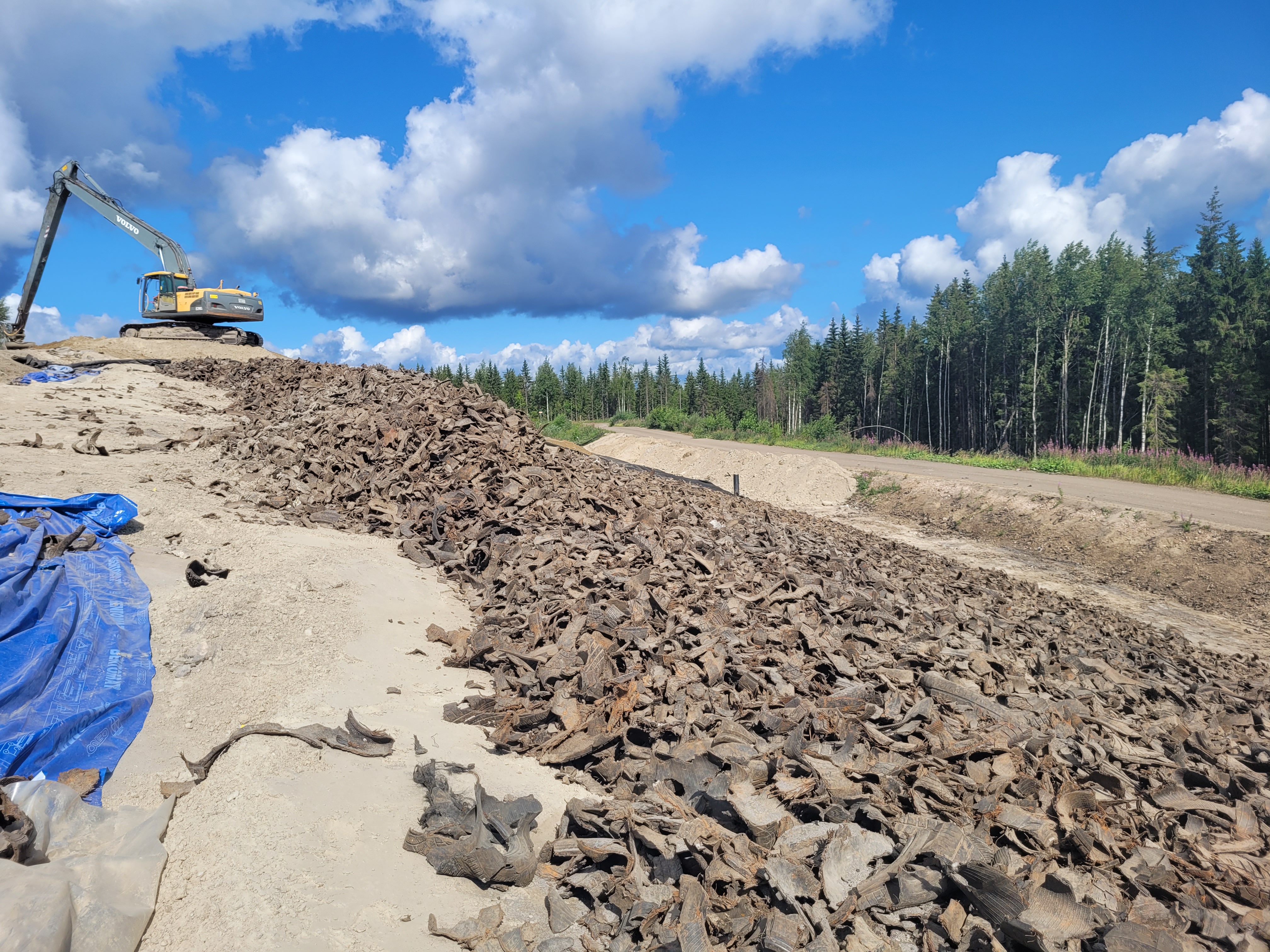 Rinteesä on pientä kumisilppua, ylhäällä kaivinkone on töissä. Taivas on kauniin sininen ja metsää näkyy oikealla.