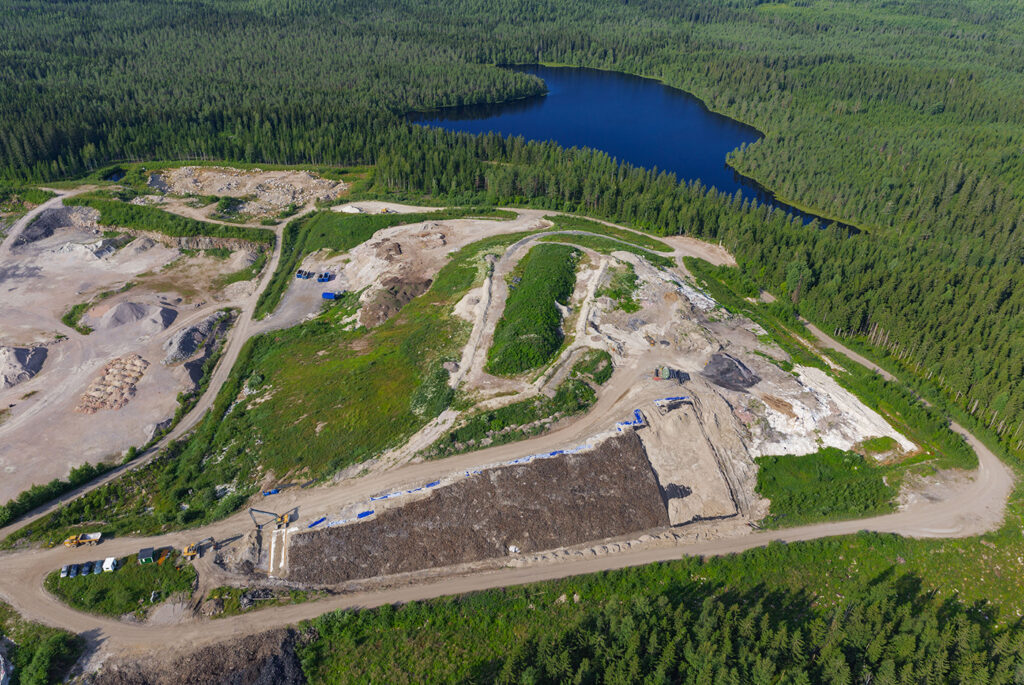 Ilmakuva, jossa näkyy jonkinlainen kukkula, jonka takana on järvi ja ympärillä metsää.