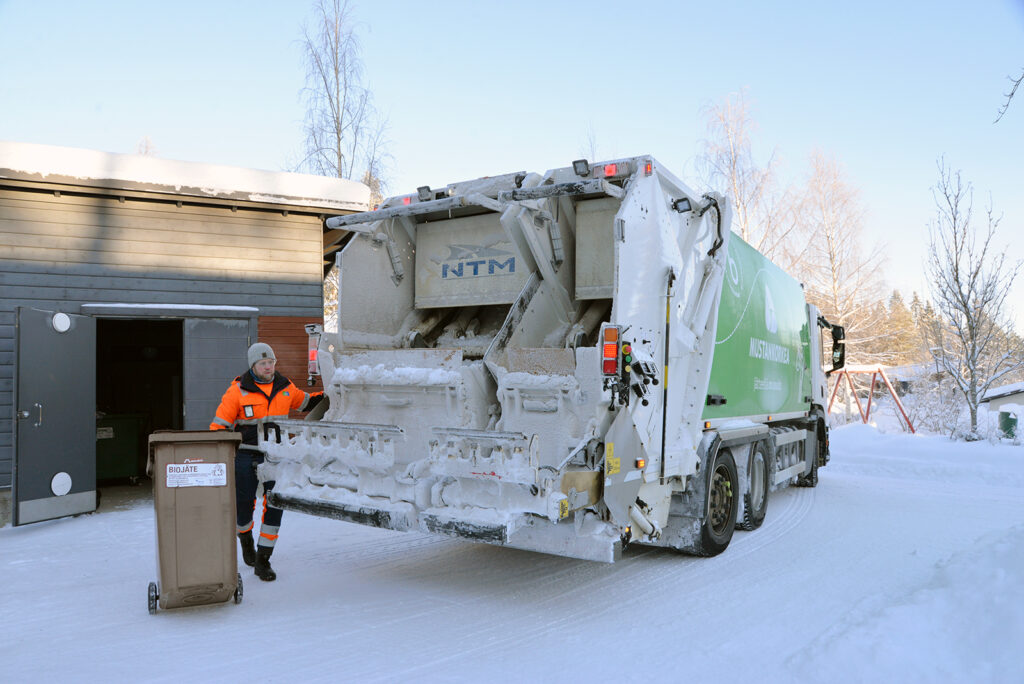 Jäteauton kuljettaja tyhjentää biojäteastiaa. On kaunis talvipäivä.