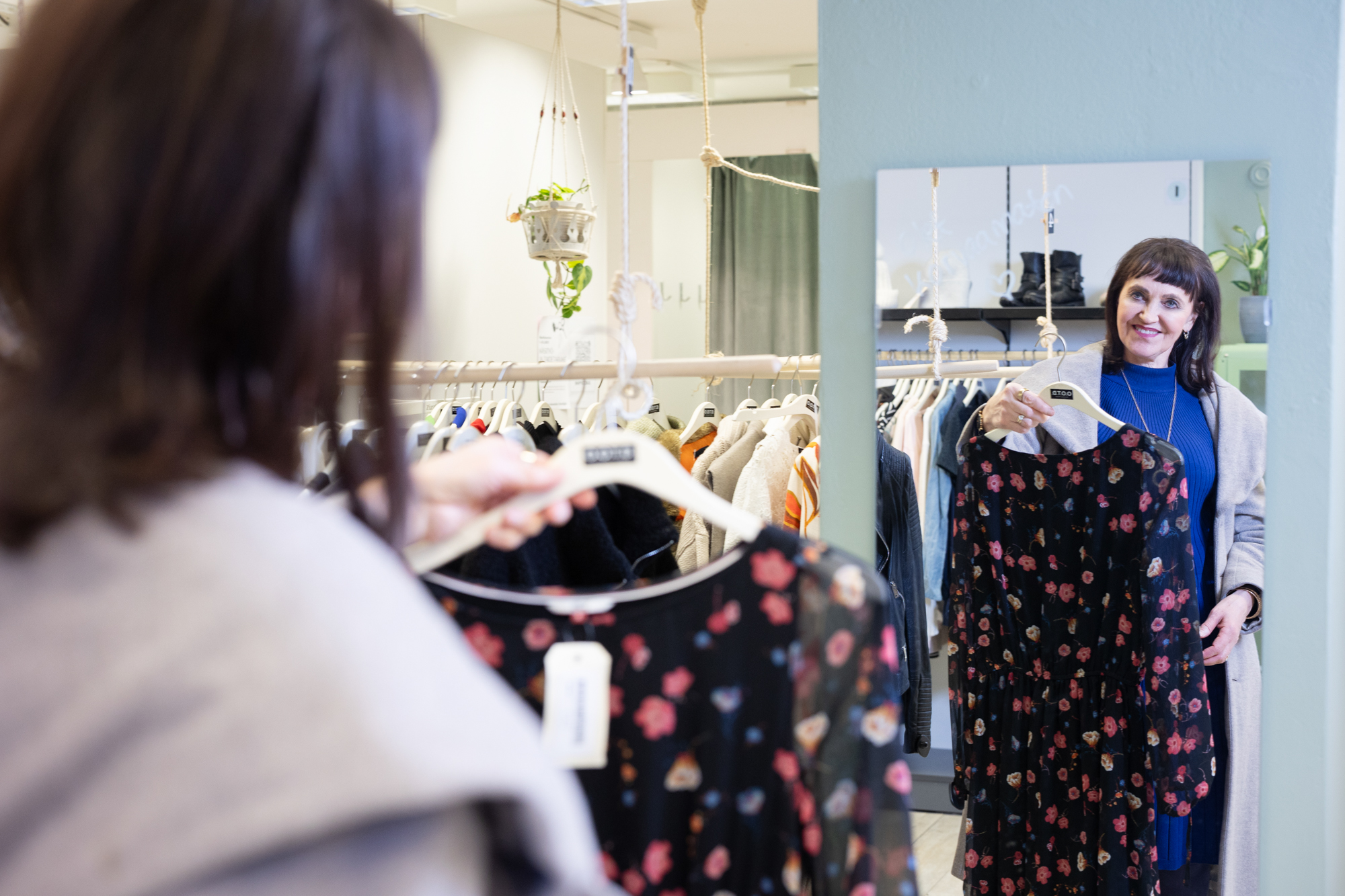 Nainen katsoo itseään peilistä hymyillen ja pitää kädessään second-hand- löytönä tehtyä mekkoa, jossa on kukkakuviointi