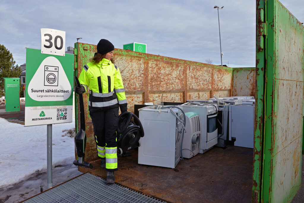 Huomiovaatteet päällä oleva nainen on imuri kädessä ja katsoo sen vieressä olevia helloja.