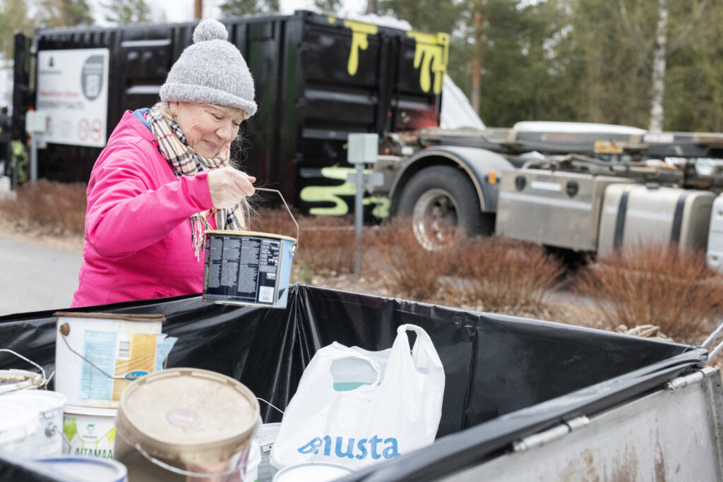 Nainen pinkissä takissa lajittelee vaarallista jätettä kierrätysautolla Toivakassa.