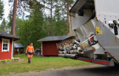 Huomiovaatteet päällä oleva mies tähyilee jonkin mökkipihan ympäristöä. Jäteauton perää näkyy oikealla.