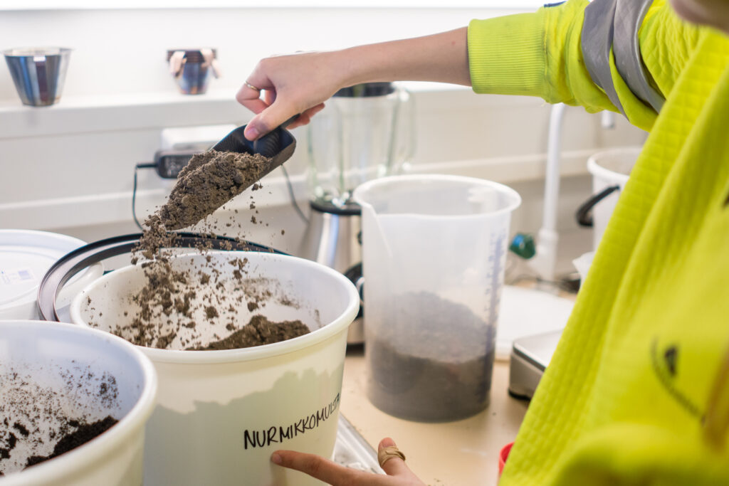 Työntekijä ottaa multanäytettä laboratoriossa nurmikkomullasta.