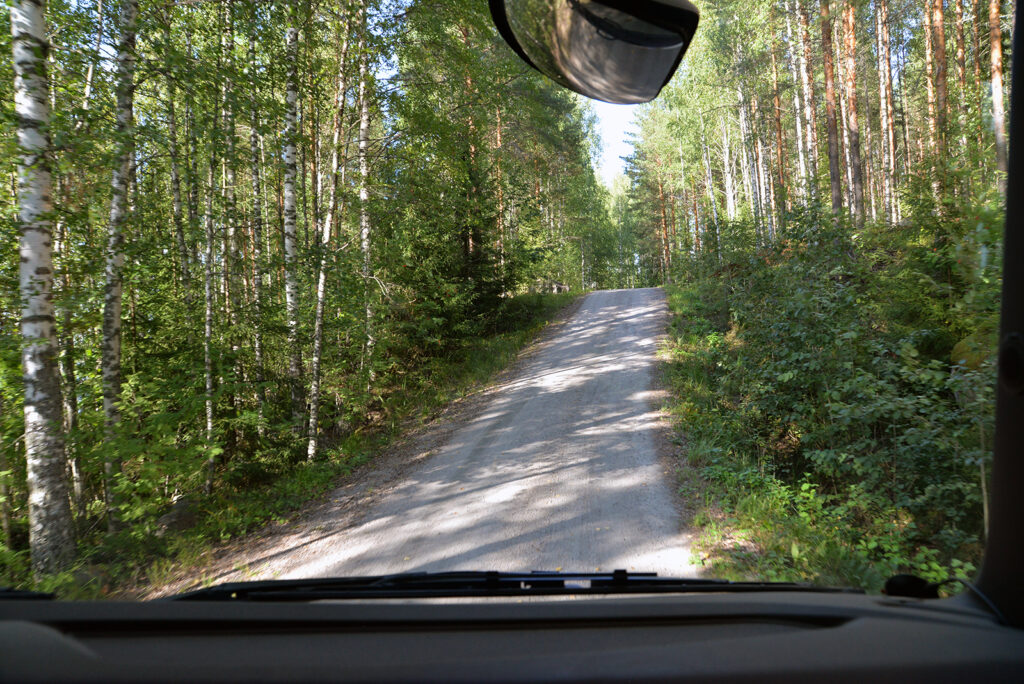 Ohjaamosta näkyy pieni hiekkatie, joka nousee mäkeä ylöspäin. Ollaan melko metsässä.