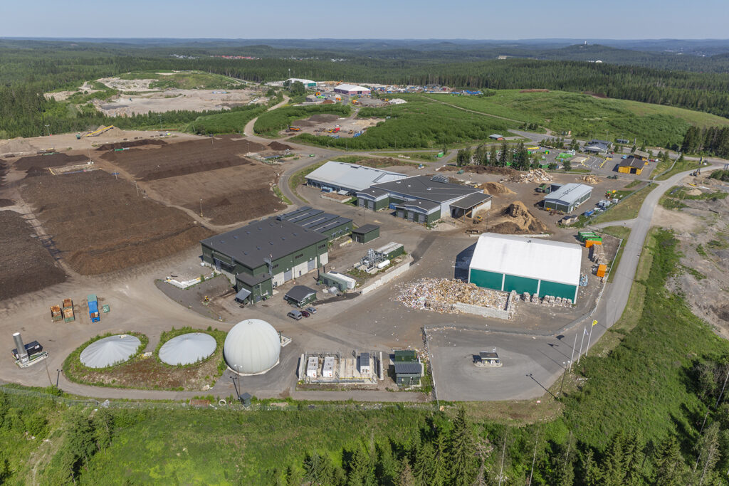 Ilmakuva, jossa näkyy erilaisia rakennuksia, kompostiaumoja ja metsää horisontissa.