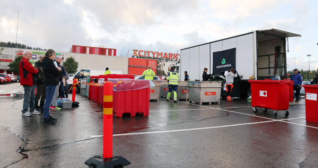 Huomiotakkiset ihmiset hääräävät kuvassa, kun toiset odottavat huomionauhan takana. Taustalla näkyy K-Citymarketia.