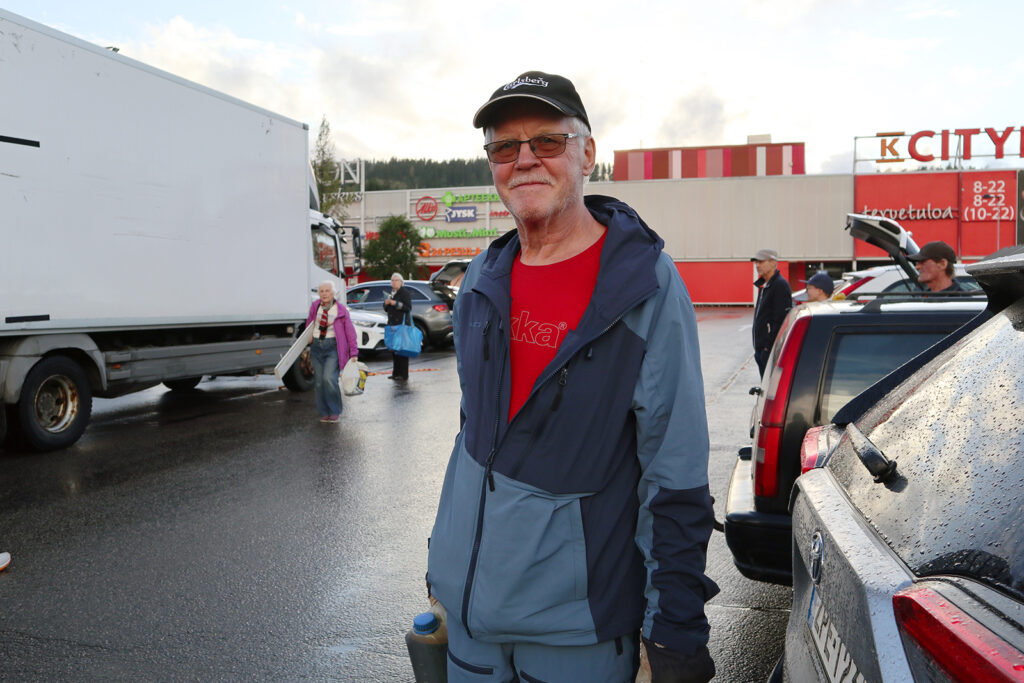 Punainen Rukan paita päällä oleva mies katsoo kameraan hieman hymyillen. Hänellä on kädessään jotain pieniä kanistereita.