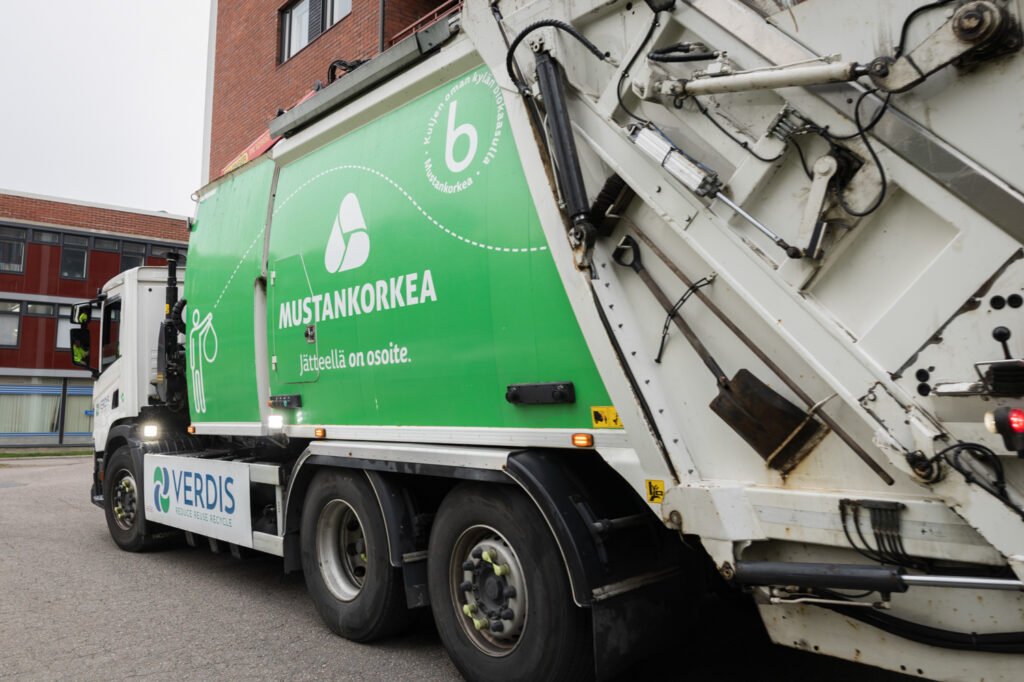 Vihreä jäteauto, jossa lukee Mustankorkea ja alempana Verdis. Taustalla näkyy punatiilistä rakennusta.
