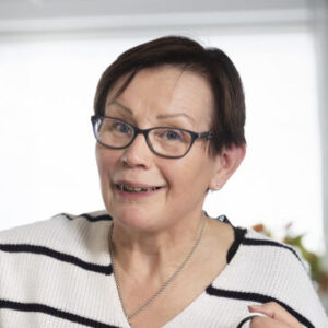 Silmälasipäinen nainen katsoo kameraan ja hymyilee.