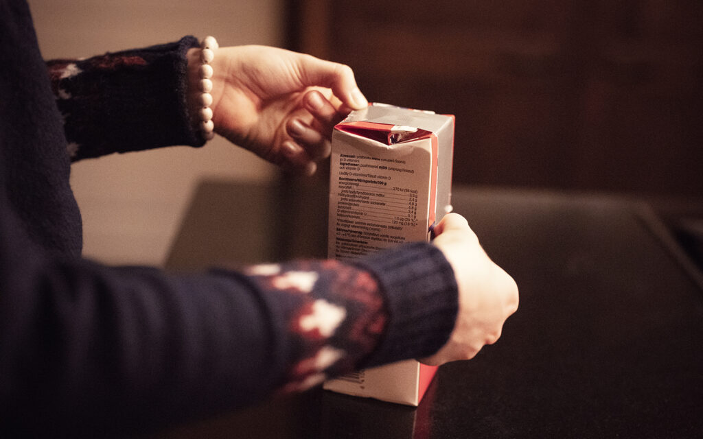 Punaista maitotölkkiä suljetaan teipillä. Kuvassa näkyy naisen kädet ja villapaitaa.