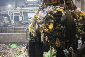 Jonkinlaisessa kauhassa on epämääräistä moskaa ja jätesäkkejä. Taustalla näkyy erilaista laitteistoa.