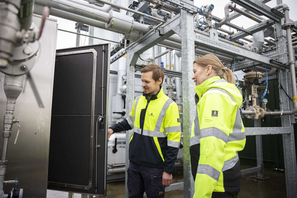 Mies ja nainen katsovat jonkinlaista avoinaista ovea. Taustalla näkyy monenlaisia teknisiä laitteita ja putkia.