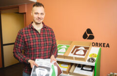 Ruutupaita päälle oleva mies pitää käsissään jäteastiatarroja. Taustalla näkyy niitä lisää hyllyssä.