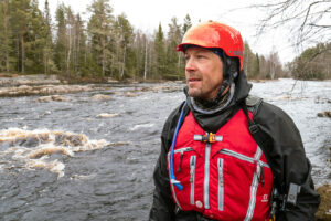 Mies on kypärä päässä kosken vieressä.