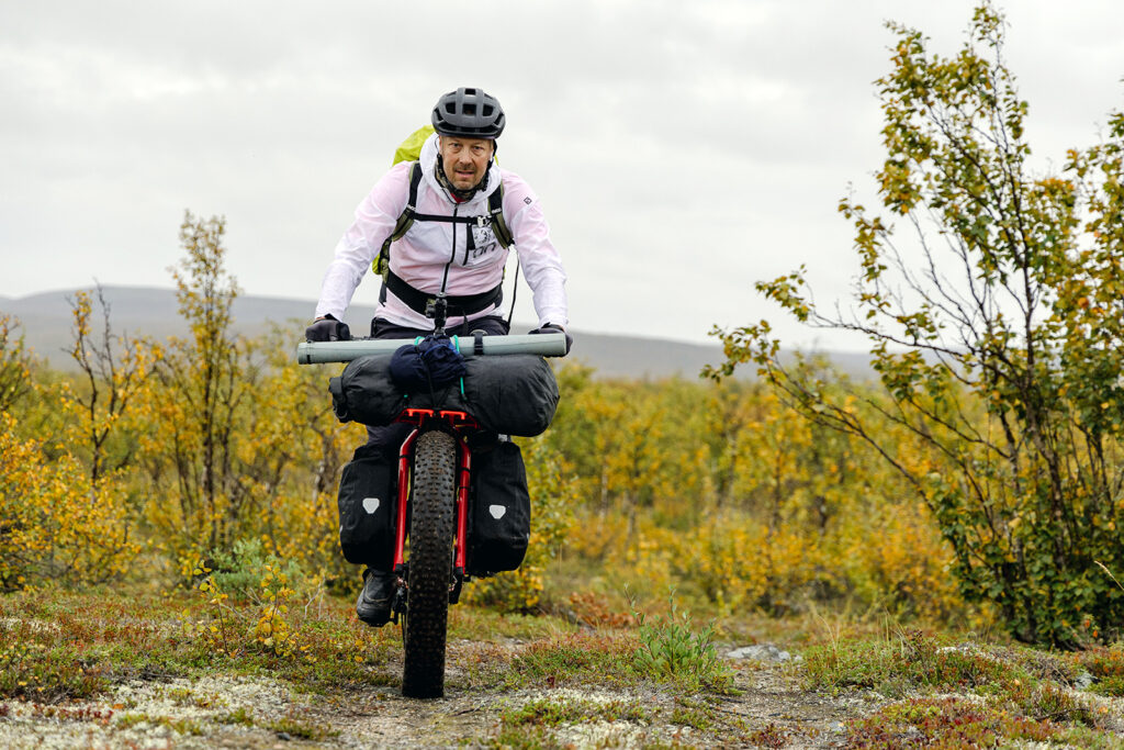 Mies on retkipyöräilemässä jossain pohjoisessa. Vuodenaika näyttää syksyltä ja hänellä on pyörän kyydissä paljon tavaraa.