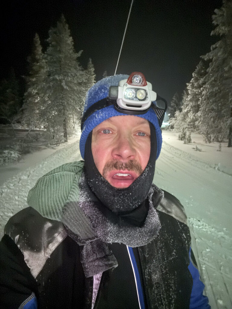 Mies on ulkona pakkasessa pimeällä. Hänellä on otsalamppu ja vaatteissa on kuuraa.