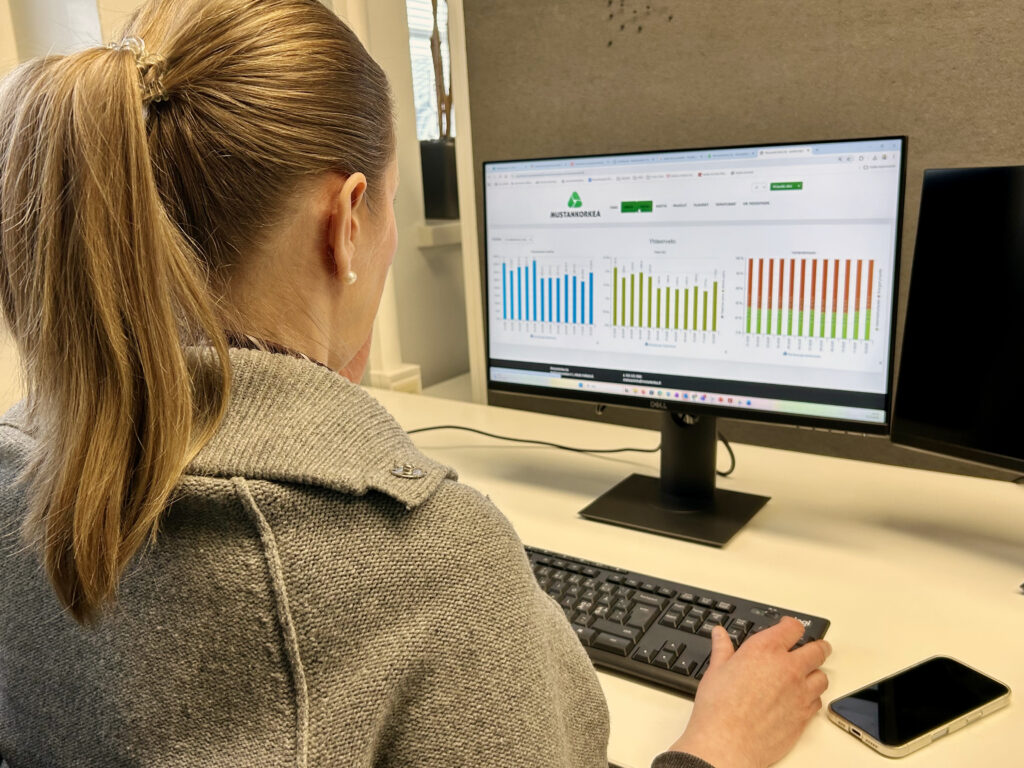 Nainen katselee tietokoneruudulta erilaisia käppyröitä. Hän on jossain toimistossa.