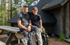 Mies ja poika ovat retkellä. Pojan käsi on isän ympärillä, takana näkyy kotaa.