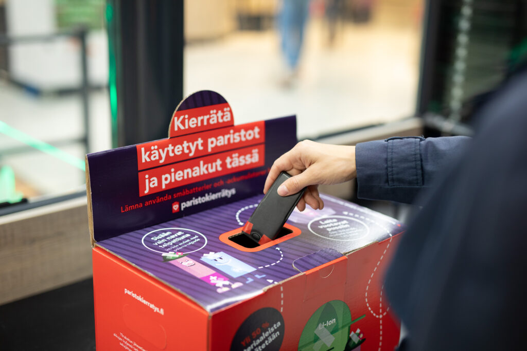 Käsi on tiputtamassa pientä akkua paristojen ja akkujen keräyslaatikkoon.