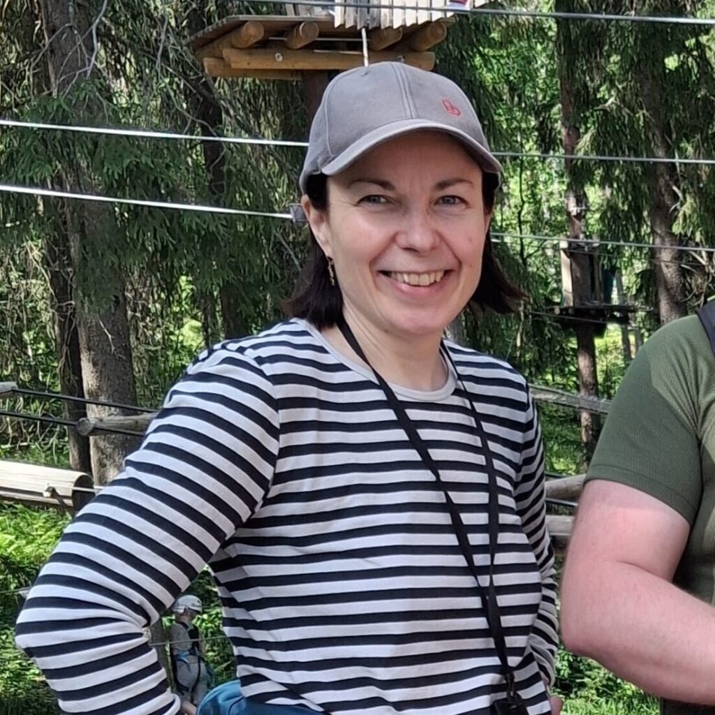 Puolikuva lippalakkisesta henkilöstä, joka hymyilee kiipeilypuiston edustalla.