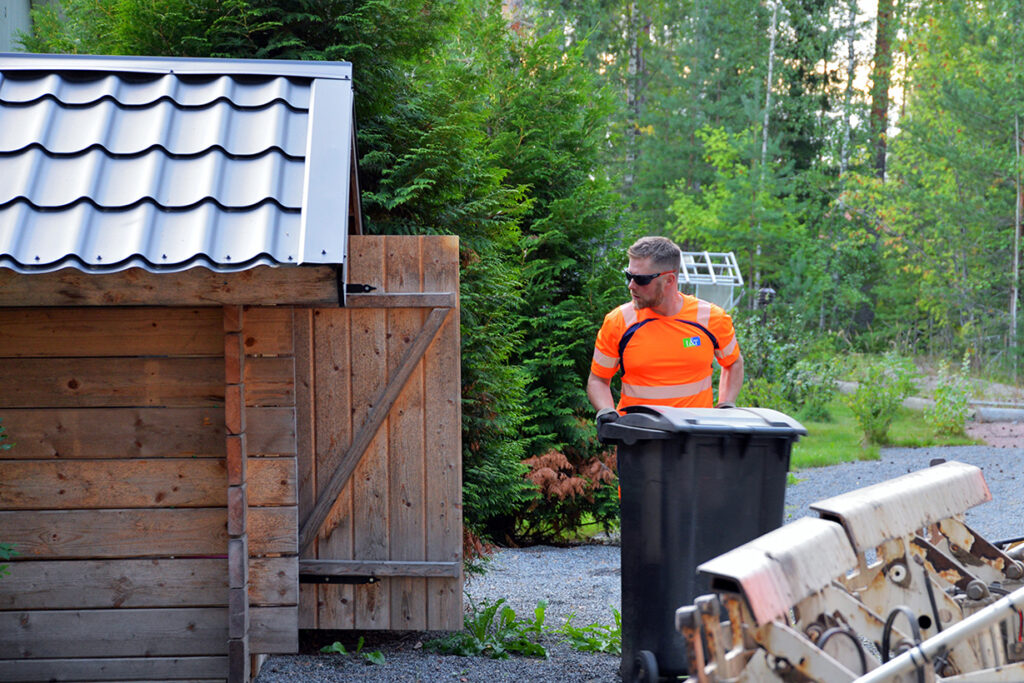 Mies tyhjentää jäteastiaa. Hänellä on päällään oranssi huomiovaatetus.