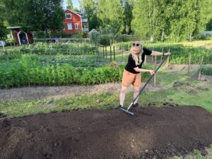 Nainen haravoi kohopenkin multaa. Taustalla näkyvät puutarha sekä punainen omakotitalo.
