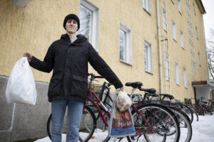 Nuori mies pitää kädessään roskapussia. Taustalla näkyy haalean keltainen kerrostalo.