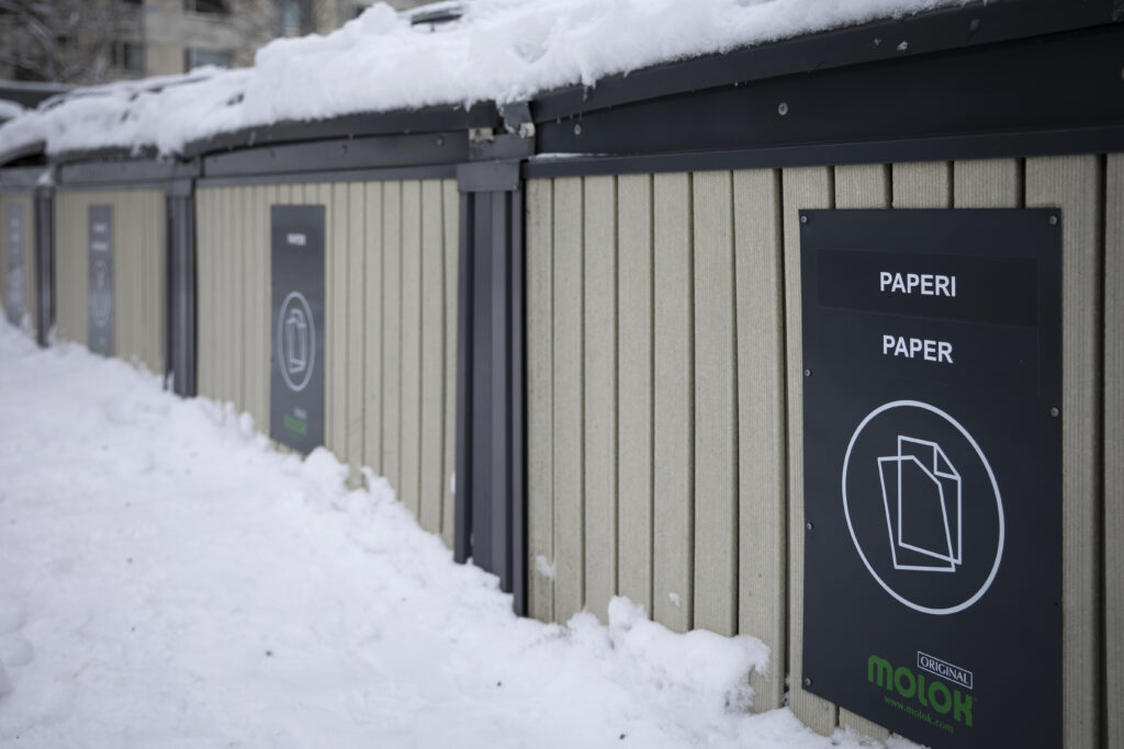 Kuvassa näkyy beigejä jäteastioita, joista etummaisessa lukee Paperi. On talvi ja lunta.